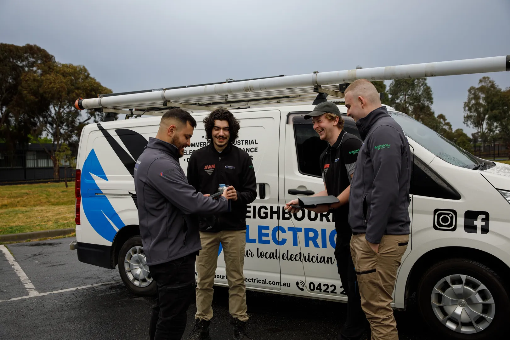 Electricians discussing near work van in parking lot.
